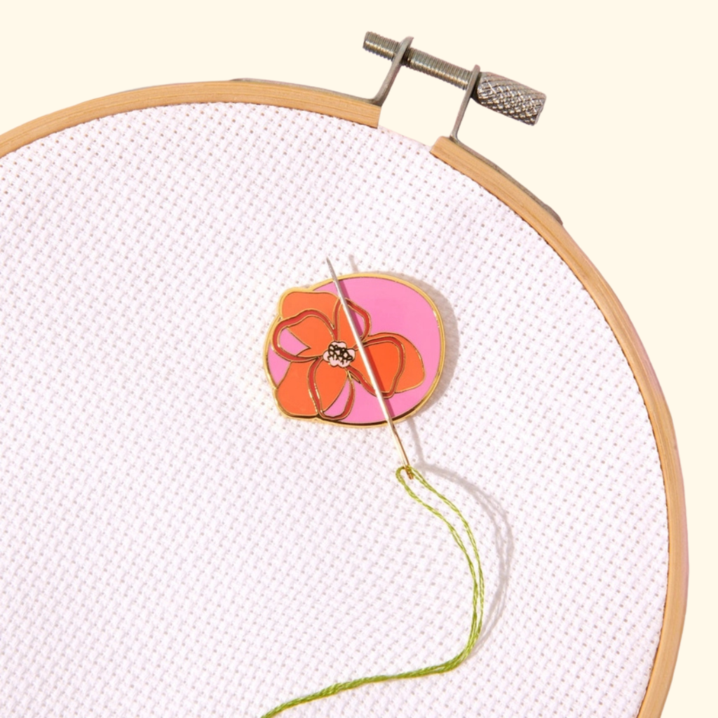 Abstract Flowers Magnetic Needle Minder by SOHMO holding a needle on floral embroidery in a wooden hoop
