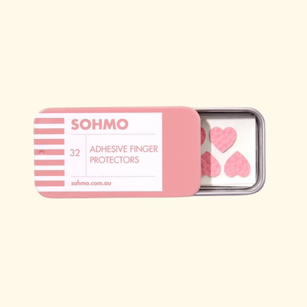 SOHMO Adhesive Thimble Pads in pink sliding-lid metal tin, partially open to reveal the protective adhesive finger pads inside.