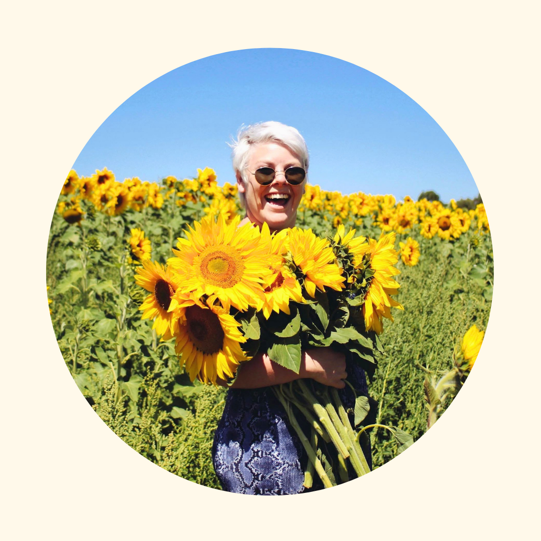 Person holding sunflowers in a field with a clear blue sky