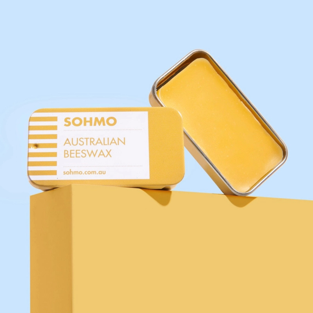 SOHMO Australian Beeswax Thread Conditioner with its gold tin lid removed, displayed on a yellow surface against a blue background.