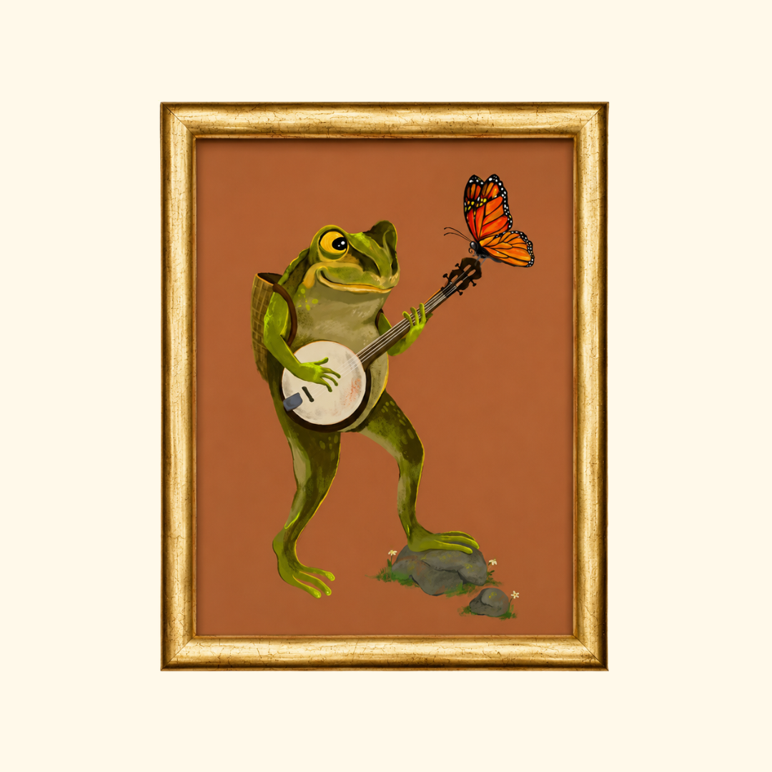 Banjo Frog greeting card displayed in a gold frame, showcasing the whimsical illustration of a green frog playing a banjo with a butterfly resting on the banjo neck.
