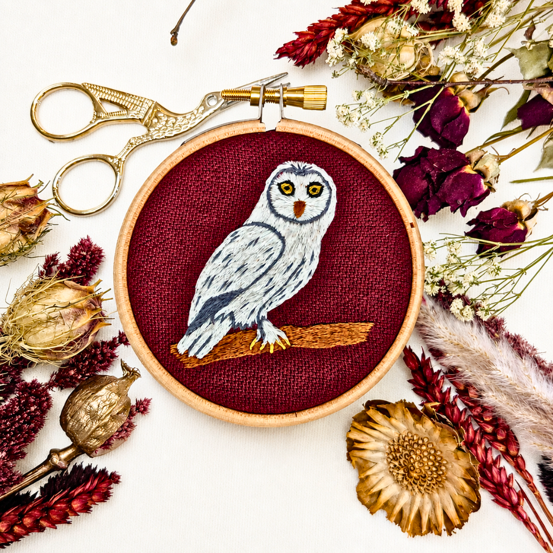 Finished snowy owl embroidery displayed with colourful threads, scissors and natural decorations.