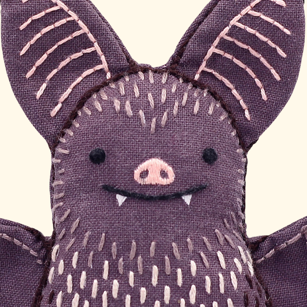 Close-up of the finished bat embroidery doll featuring large stitched ears, a pink nose and patterned body.