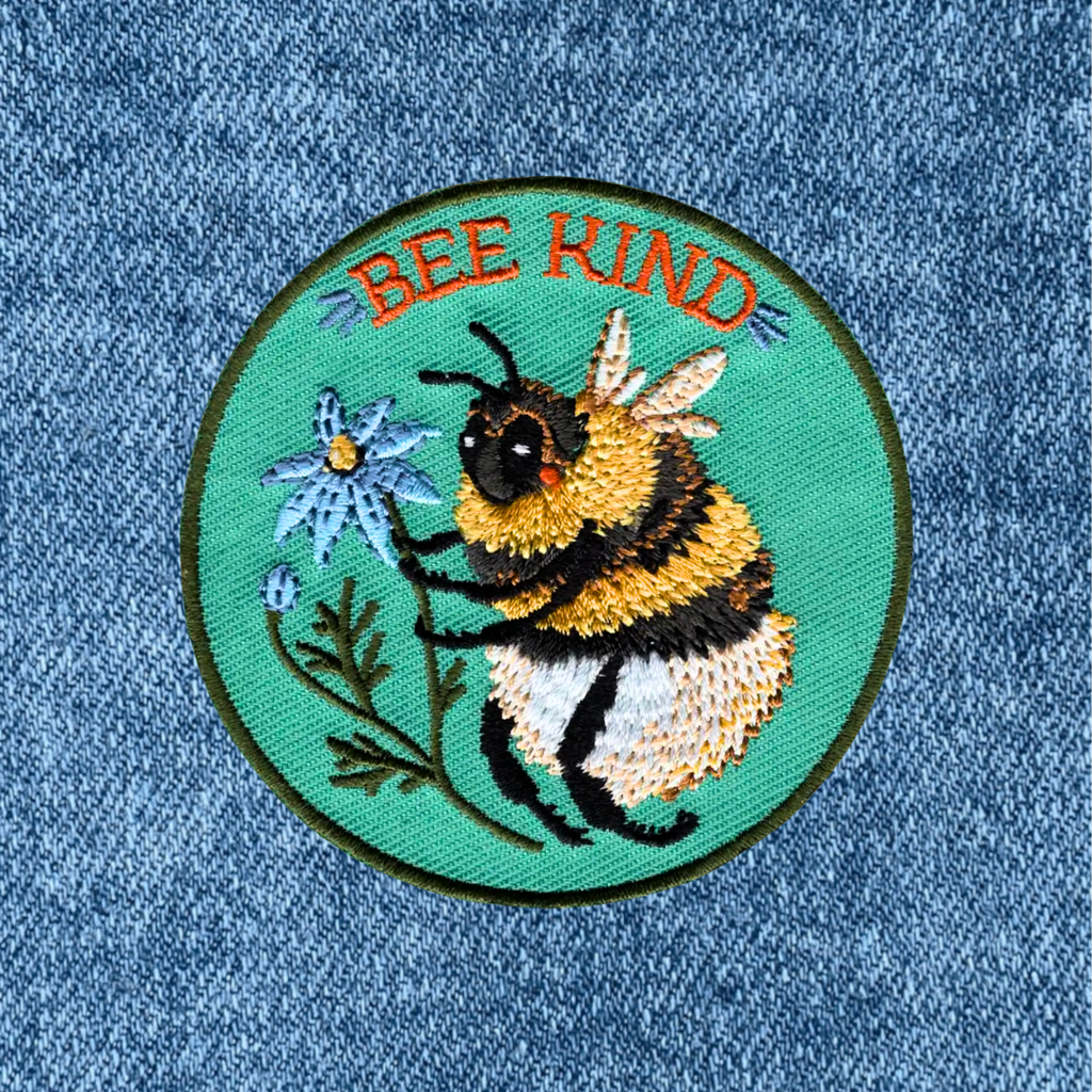 Bee Kind embroidered iron on patch by Anna Seed Art applied to blue denim fabric.