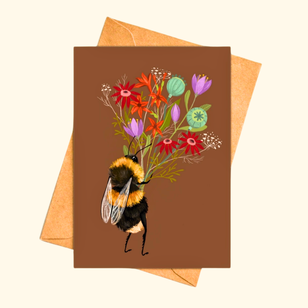 Bee With A Posy greeting card shown with a matching kraft envelope, featuring a charming bumblebee carrying a vibrant bouquet of colourful wildflowers.