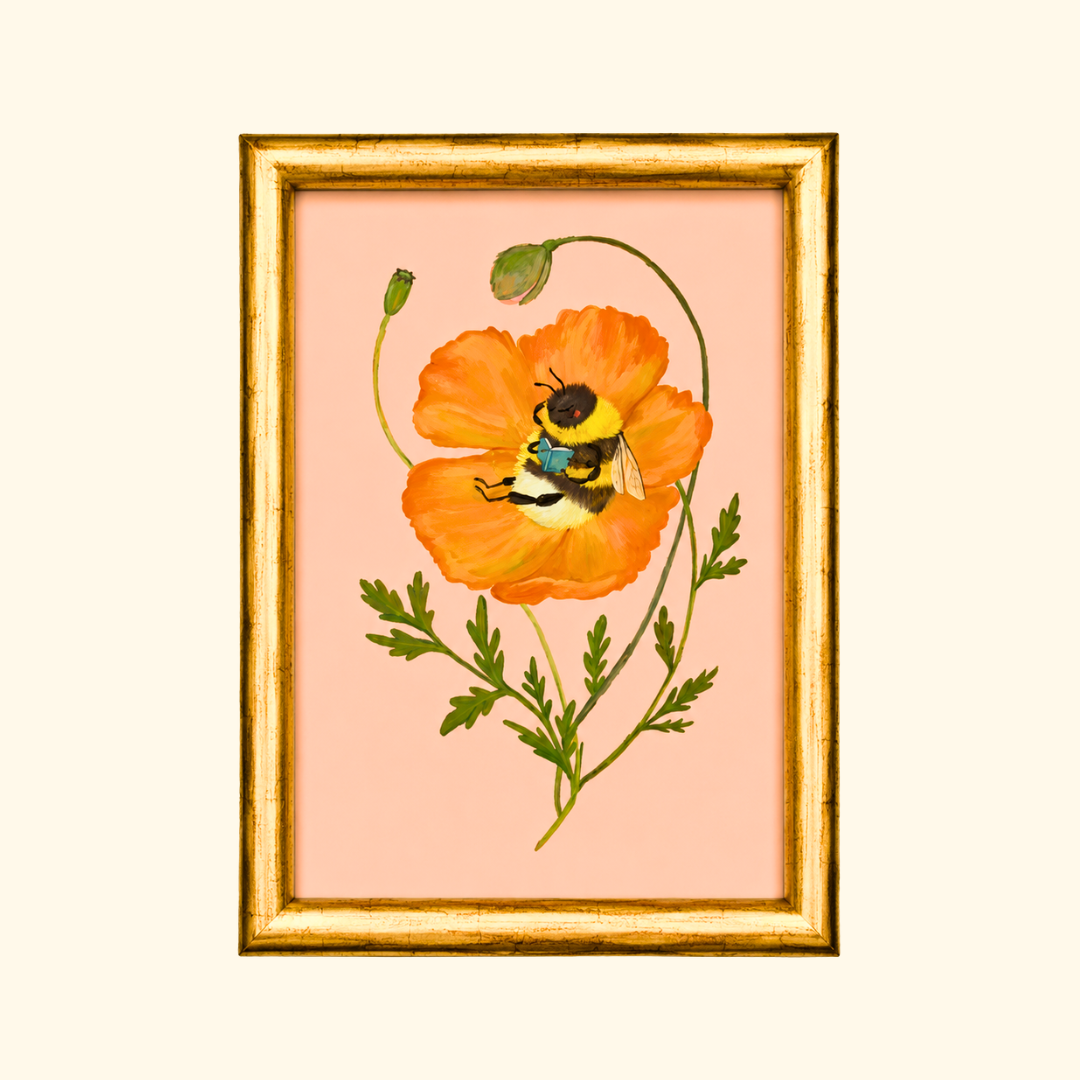 Beebliophile greeting card displayed in a gold frame, showcasing the whimsical illustration of a bee reading a book inside a blooming orange poppy.