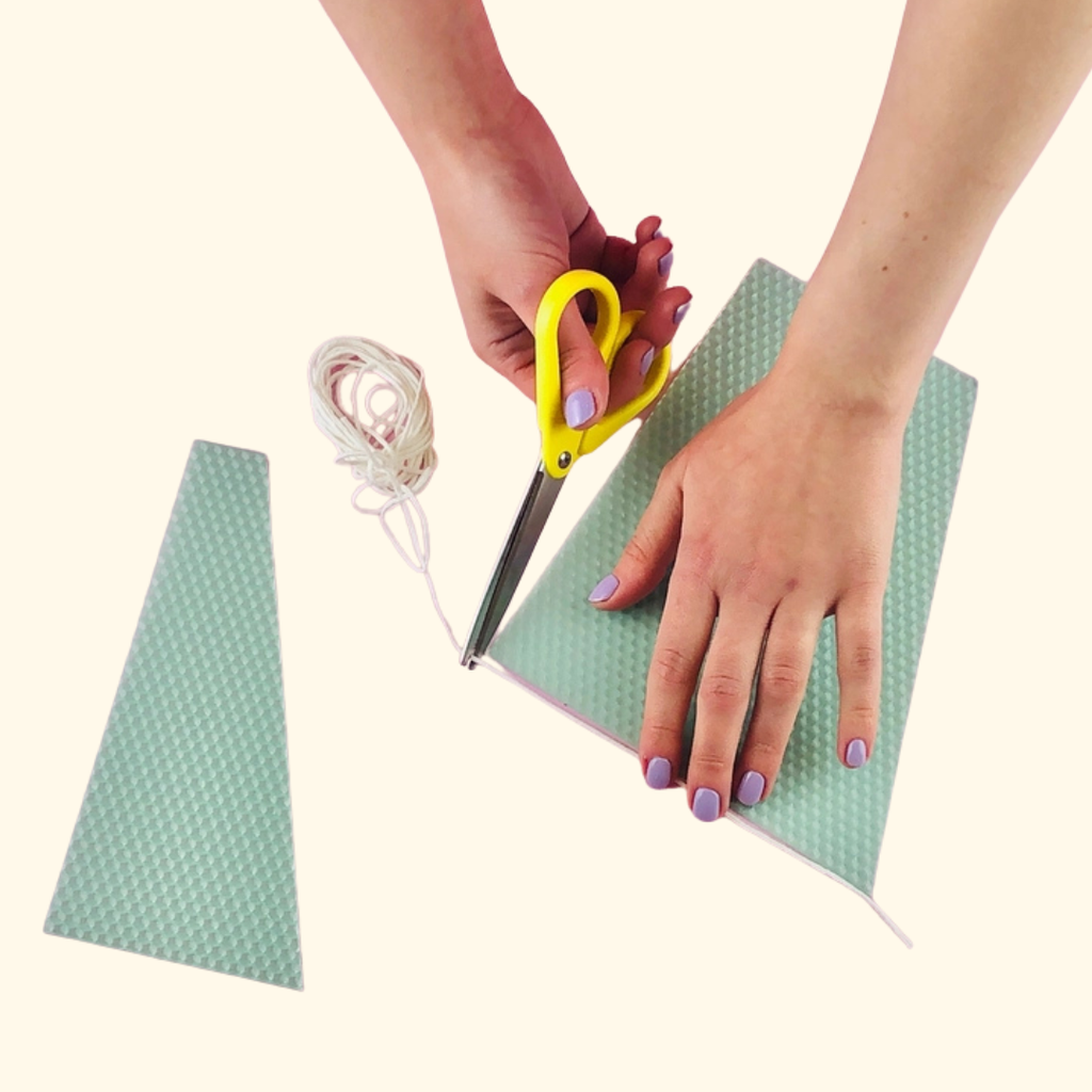 Hands rolling a sheet of beeswax around a candle wick to create a handmade beeswax candle.