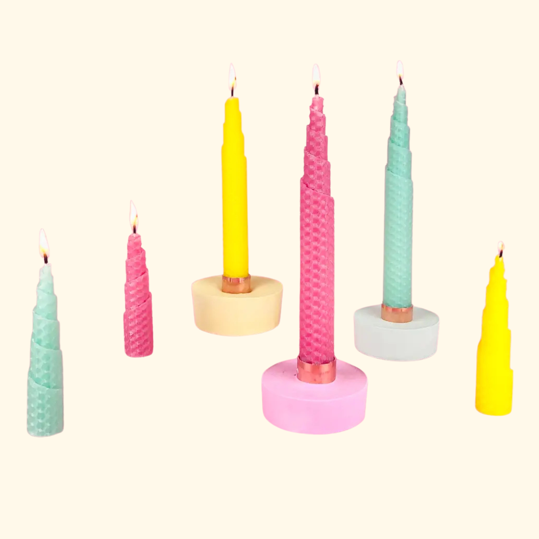 Finished hand-rolled beeswax candles in a variety of pastel colours displayed on matching candle holders.