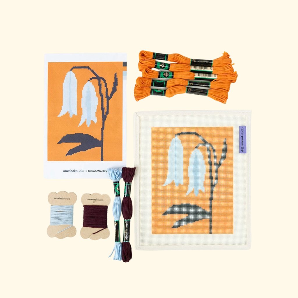 Bellwort needlepoint in progress surrounded by orange, blue, black and cream threads
