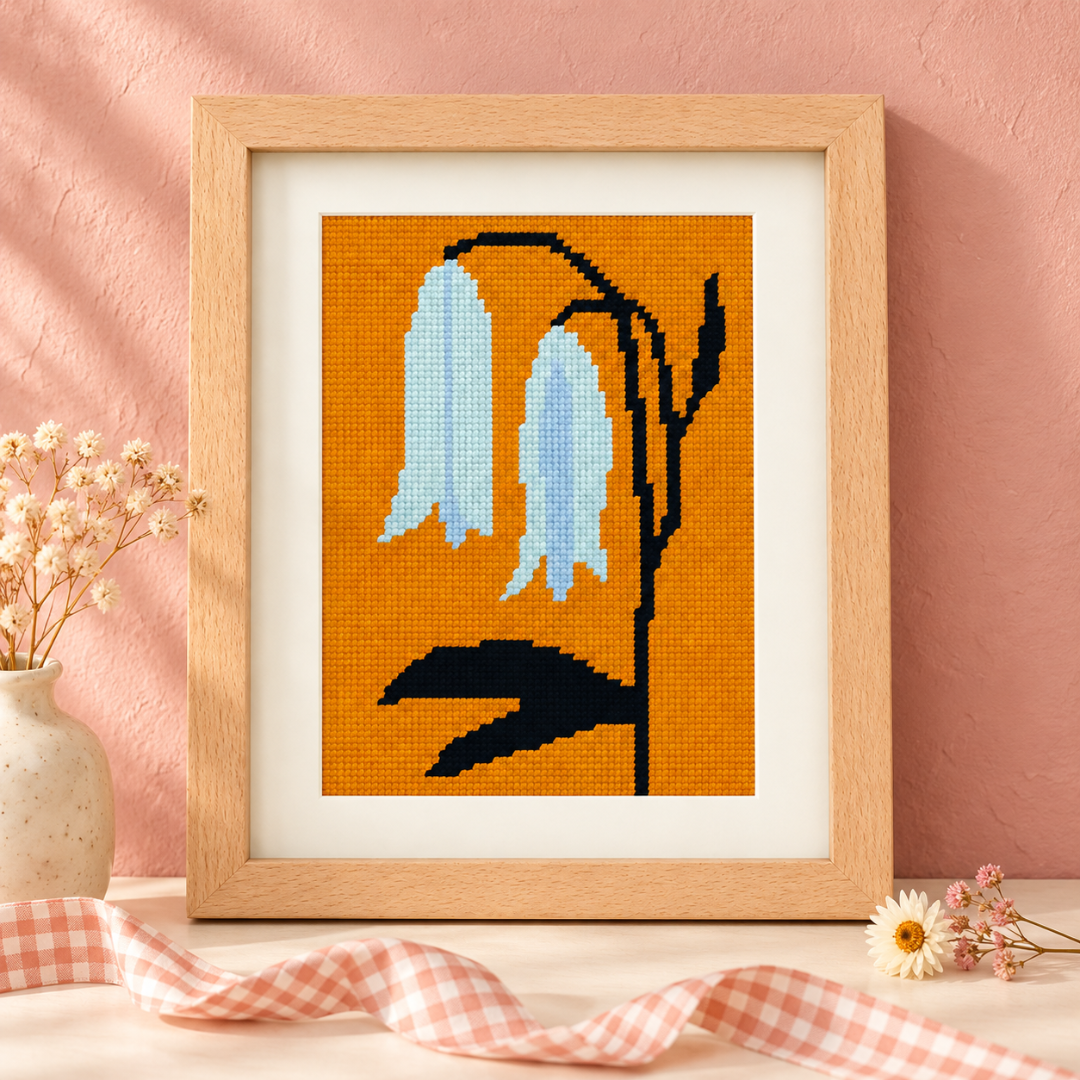 Framed bellwort floral needlepoint displayed against a soft pink background