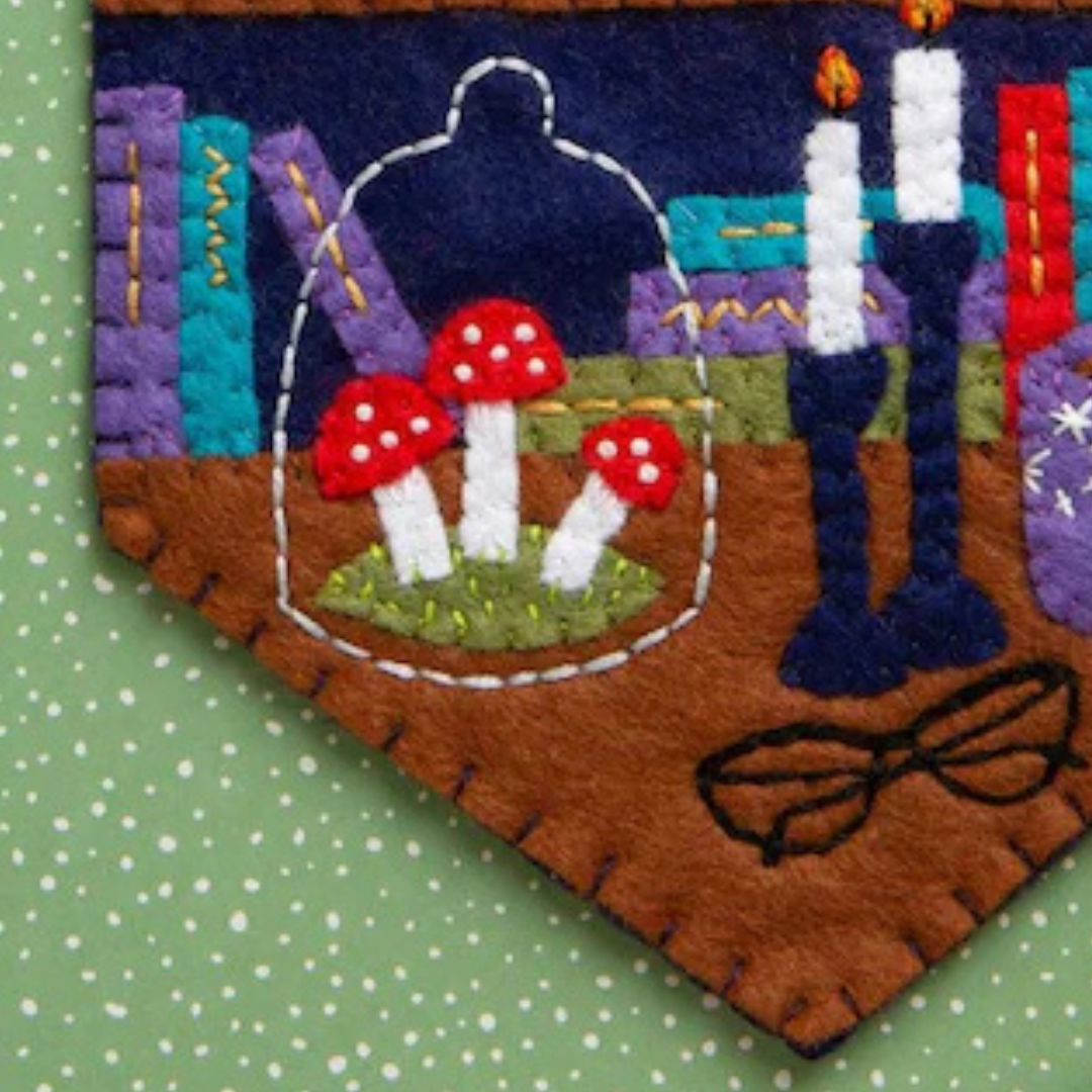 Close up of the felt bookshelf scene featuring books, candles, plants and red toadstools