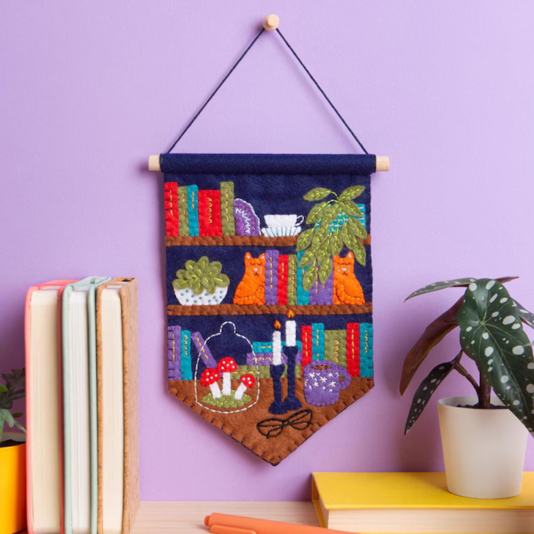 Book Nook felt wall hanging displayed on a wall beside books and a potted plant