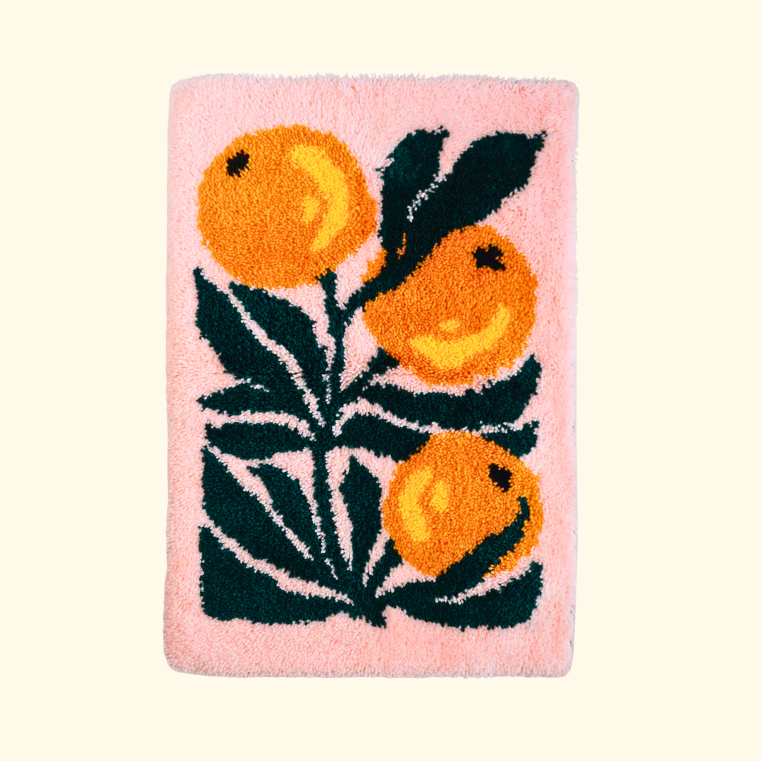 Finished latch hook rug featuring bright oranges, green leaves and a pink background, created with a latch hook kit for beginners.