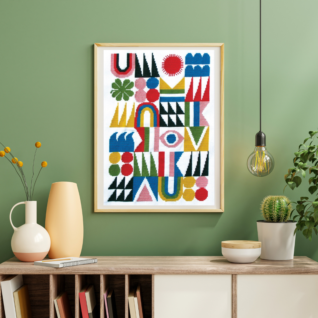 Framed Brightside Grid cross stitch design by Budgie Goods displayed on a shelf against a green wall.