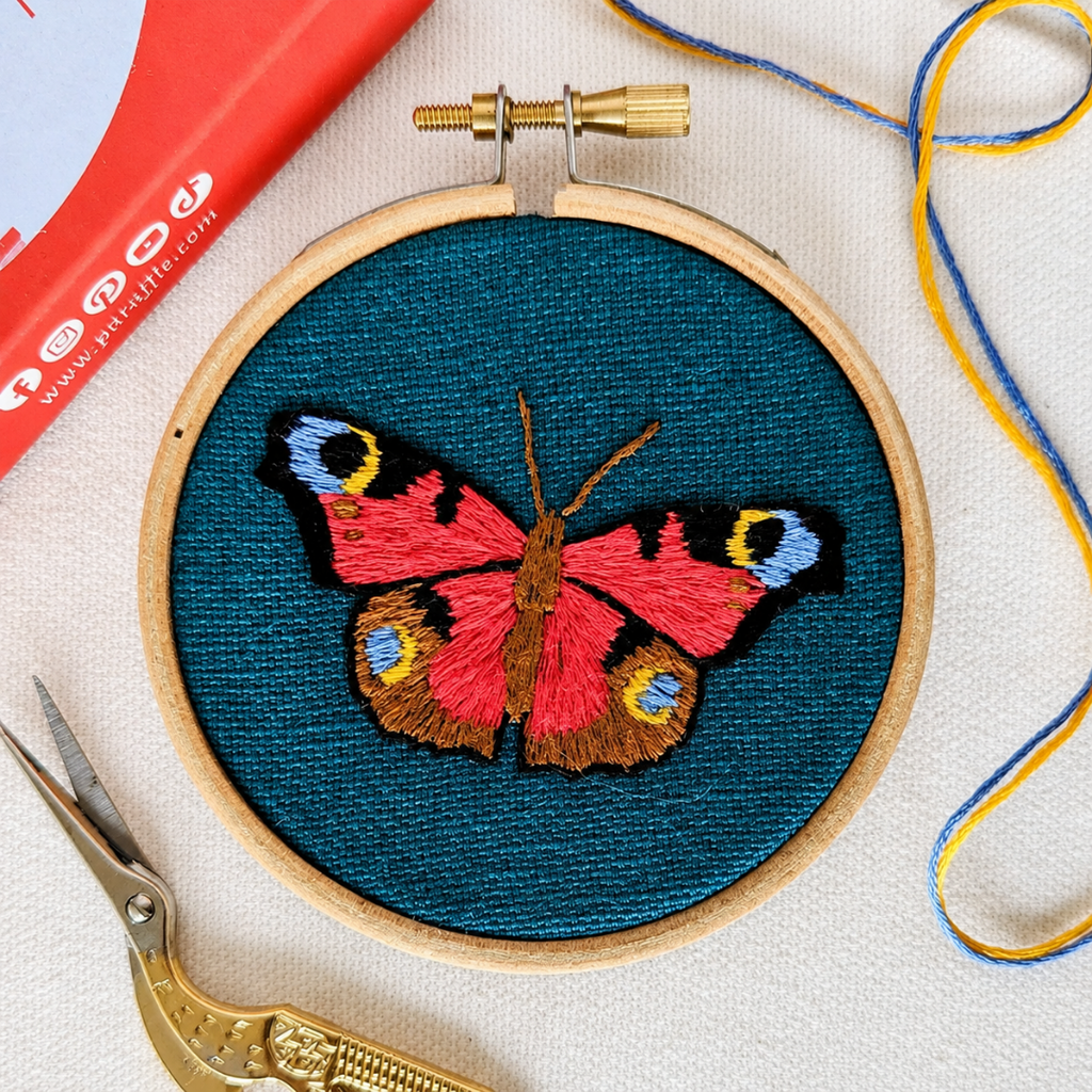 Finished butterfly embroidery displayed with embroidery tools and colourful thread.