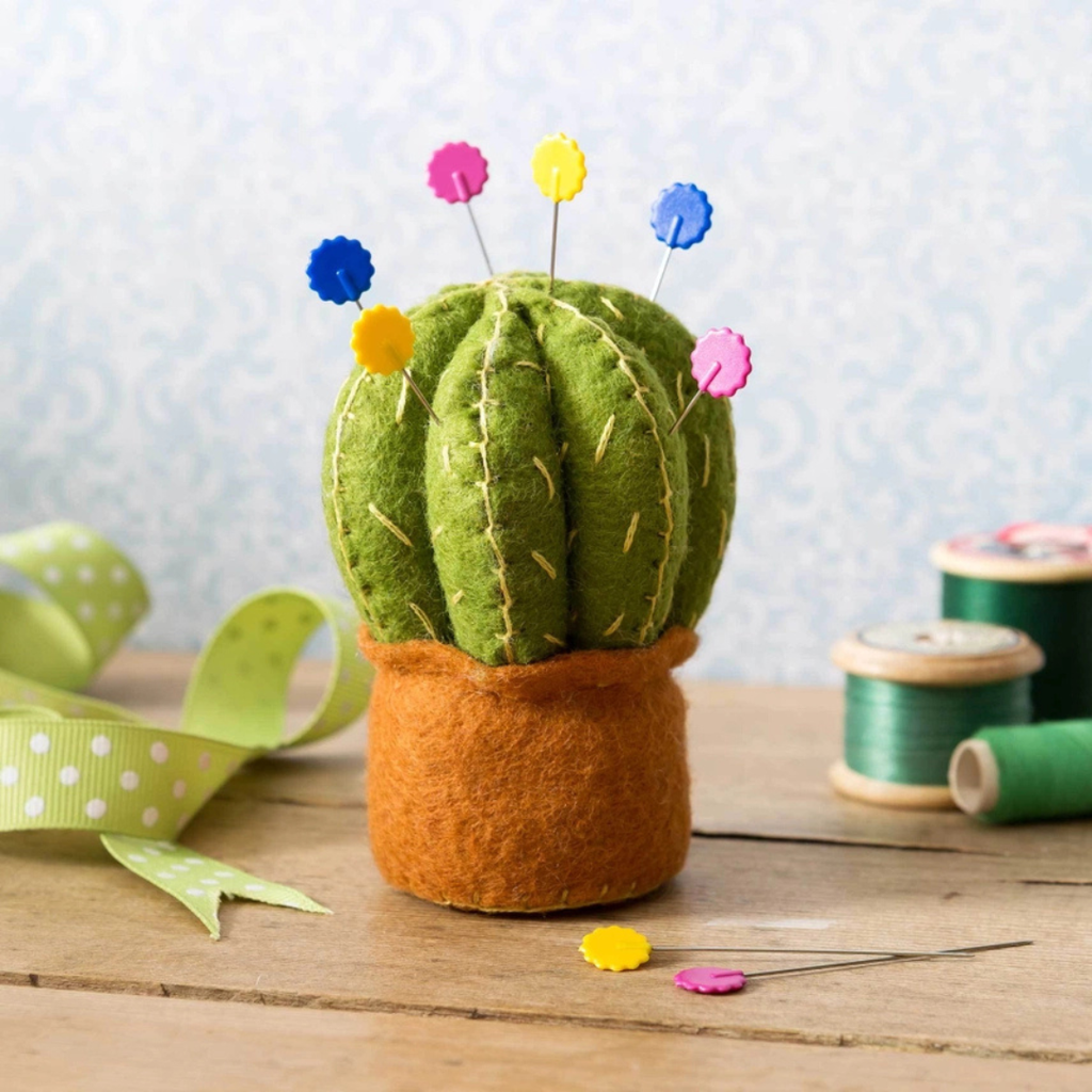 Completed Cactus Pincushion Felt Craft Kit displayed on a craft table with sewing accessories and colourful pins.