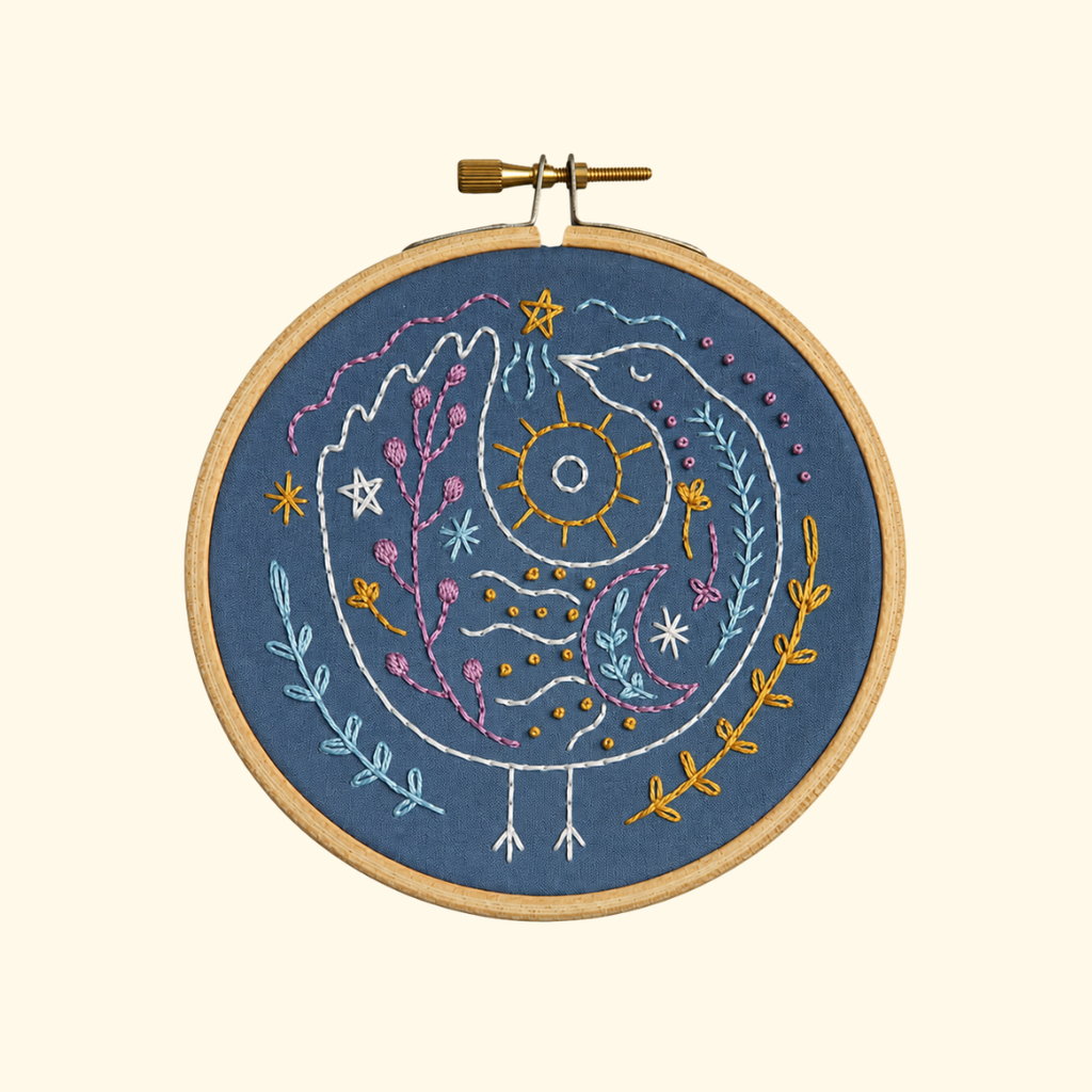 Finished Celestial Bird Mini Embroidery Kit featuring a blue and gold celestial bird design displayed in a wooden embroidery hoop.