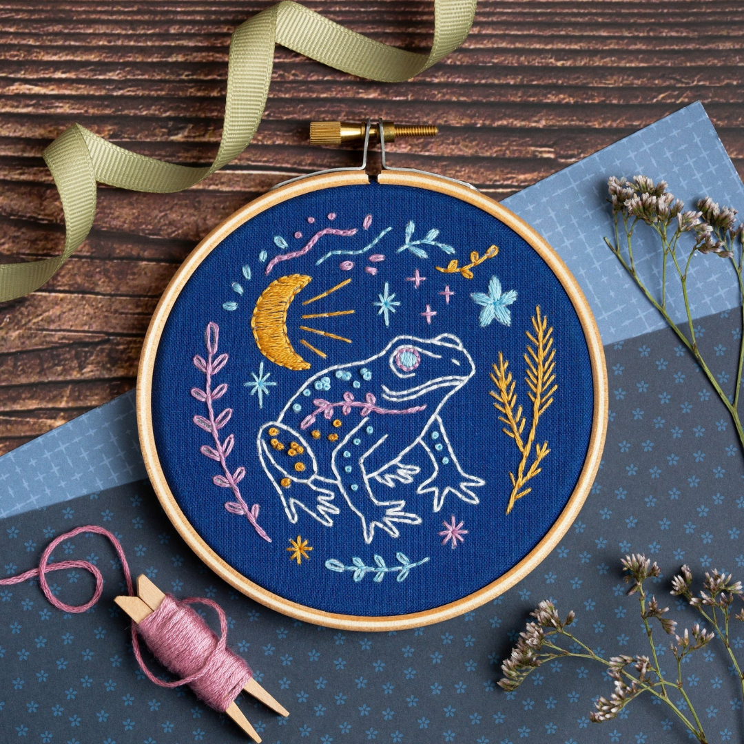 Celestial Frog Mini Embroidery Kit by Hawthorn Handmade with the finished embroidery hoop displayed on a crafting surface.