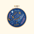 Celestial whale embroidery design stitched in a wooden hoop featuring stars, moons and botanical details on a cream background.