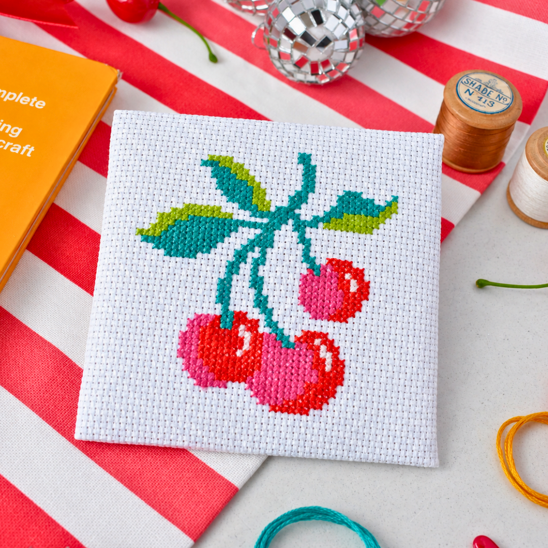 Completed cherry cross stitch design displayed with colourful craft supplies.
