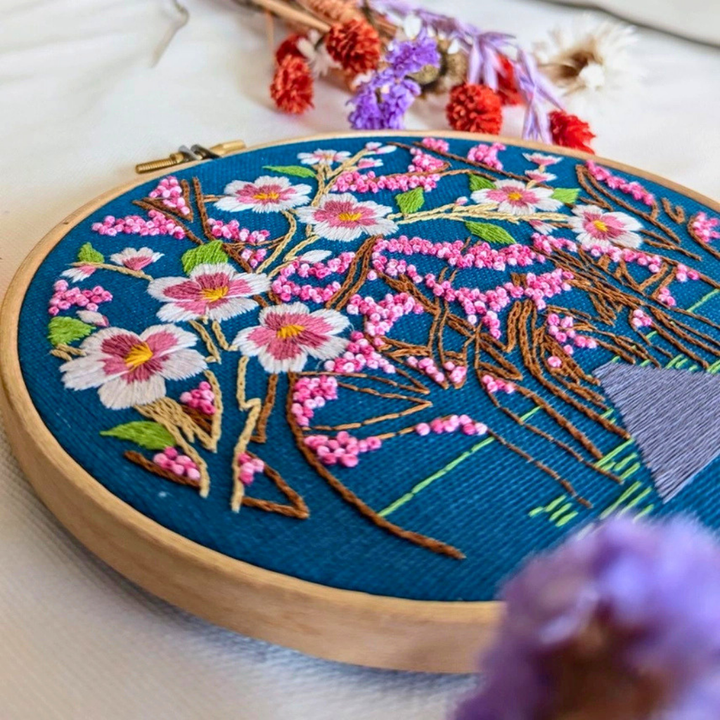 Close-up angled view of pink cherry blossom branches embroidered on blue fabric.