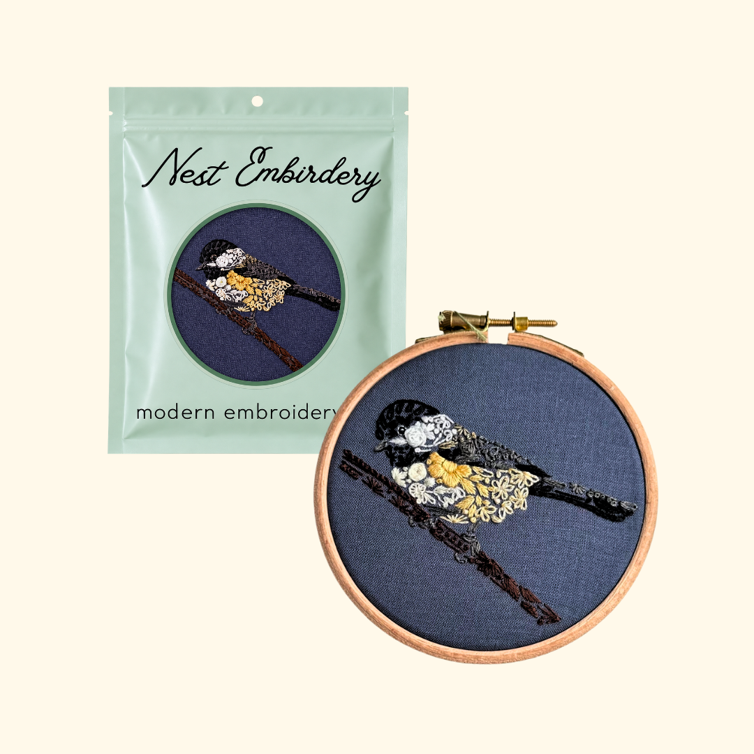 Nest Embirdery Chickadee Mini Embroidery Kit packaging displayed alongside the completed bird embroidery in its wooden hoop.