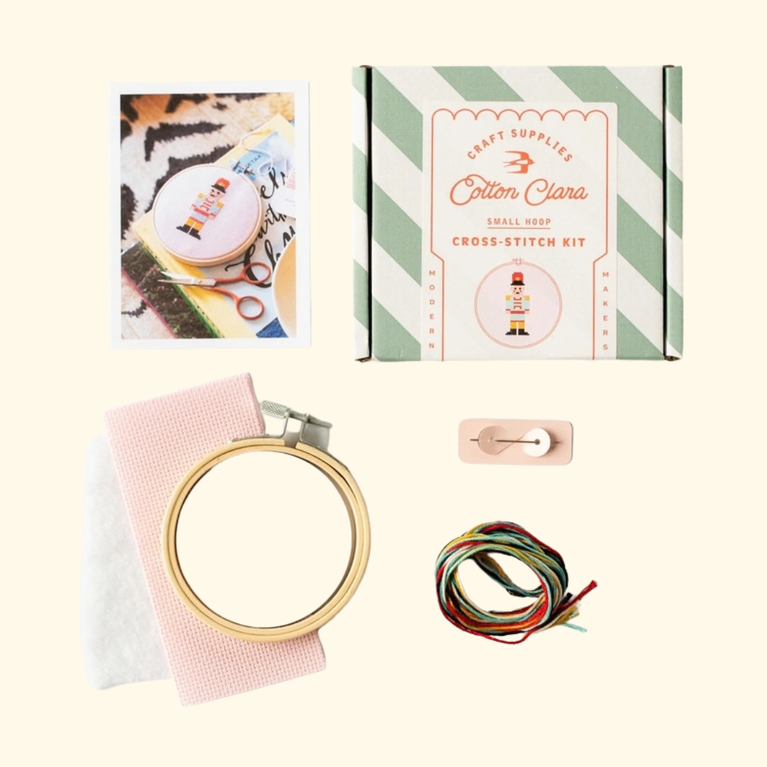Contents of the Cotton Clara Christmas Nutcracker Cross Stitch Kit including hoop, pink Aida fabric, embroidery threads, needle and instructions.