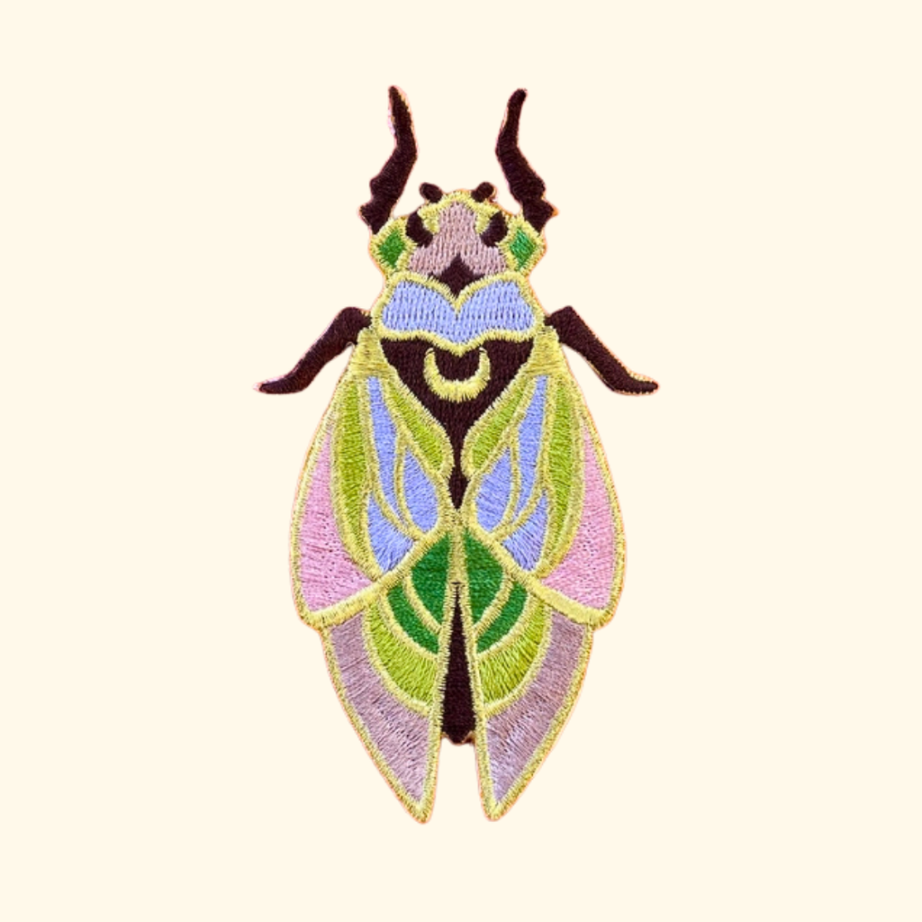 Colourful cicada embroidered iron on patch by Ashlea Bechaz Illustration featuring green, pink, yellow and purple stitching, detailed wings and dark antennae on a cream background.