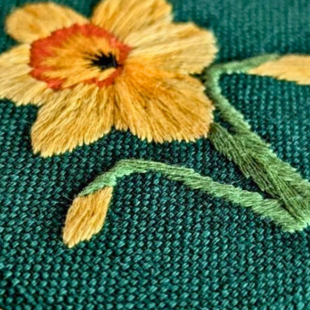 Close-up of the completed yellow daffodil mini embroidery design stitched on green fabric.