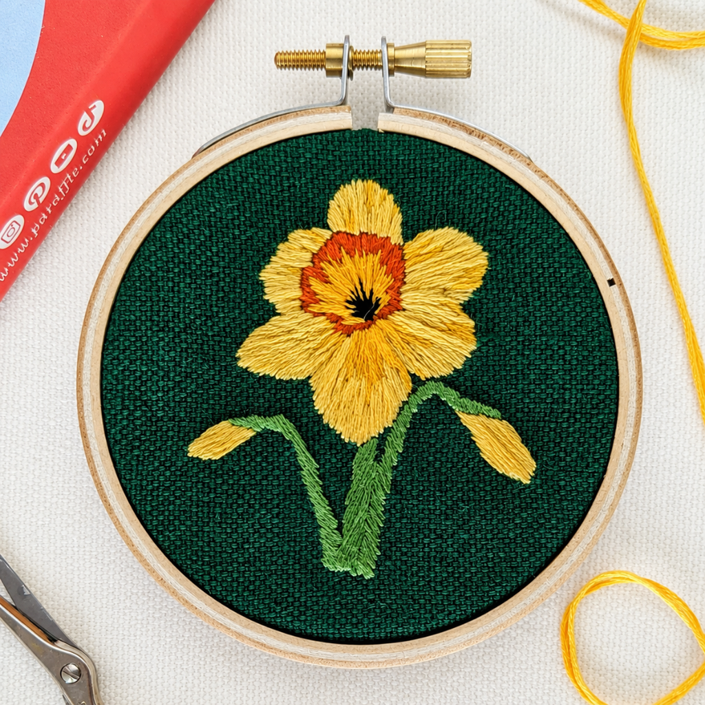 Finished daffodil embroidery displayed with embroidery tools and yellow thread.