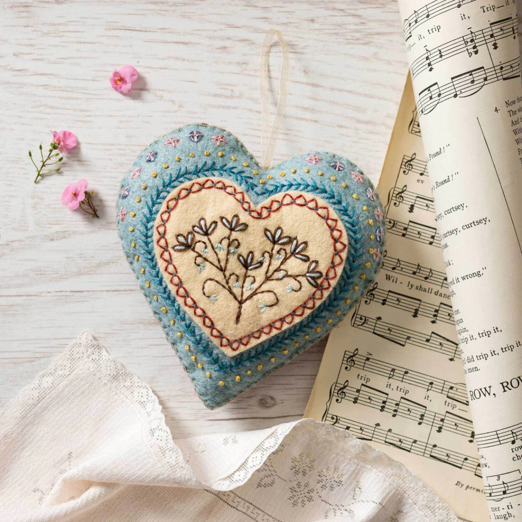 Finished embroidered heart ornament from the Corinne Lapierre felt craft kit styled with fabric and book pages.