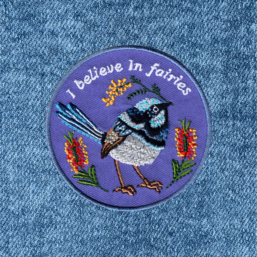 Fairy Wren embroidered iron on patch by Anna Seed Art applied to blue denim fabric.