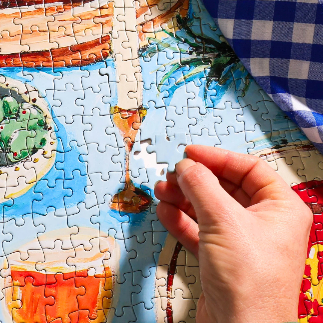 Close up detail of the Feast on the Sunlit Terrace 1000 piece puzzle with hand placing a puzzle piece.
