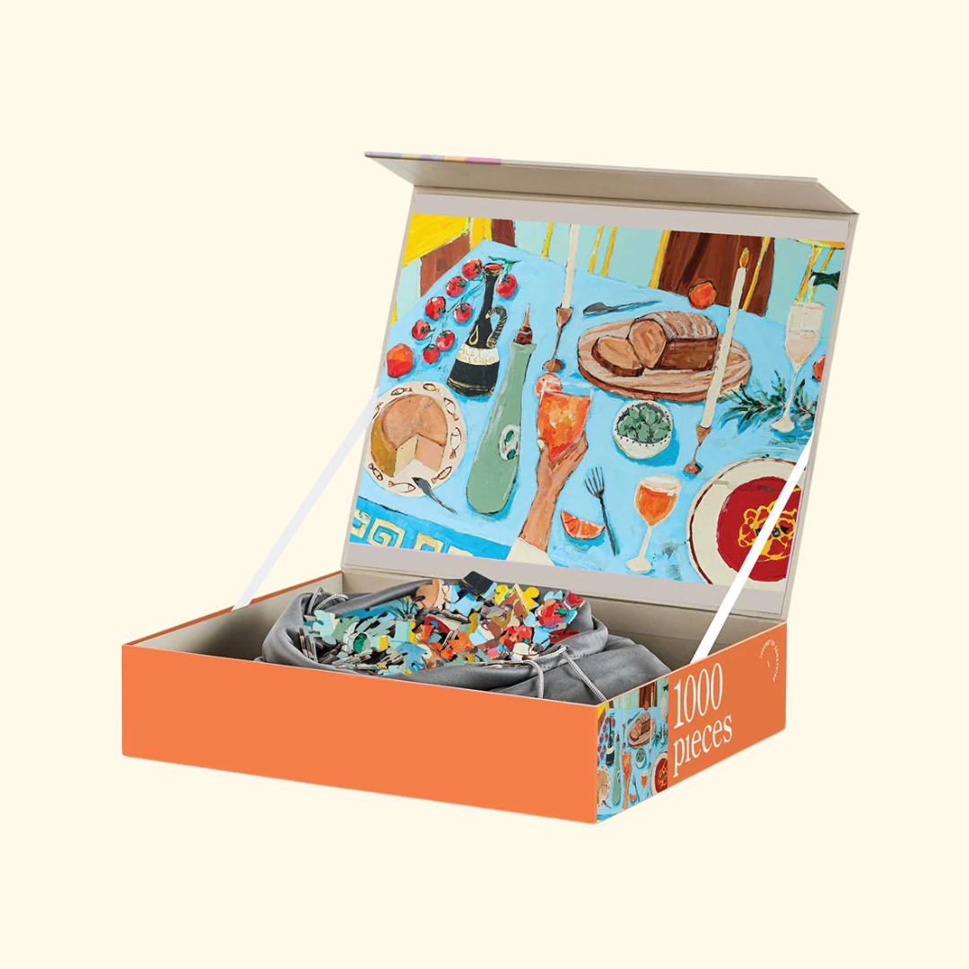 Open box of the Feast on the Sunlit Terrace 1000 piece puzzle with drawstring puzzle bag and artwork inside.