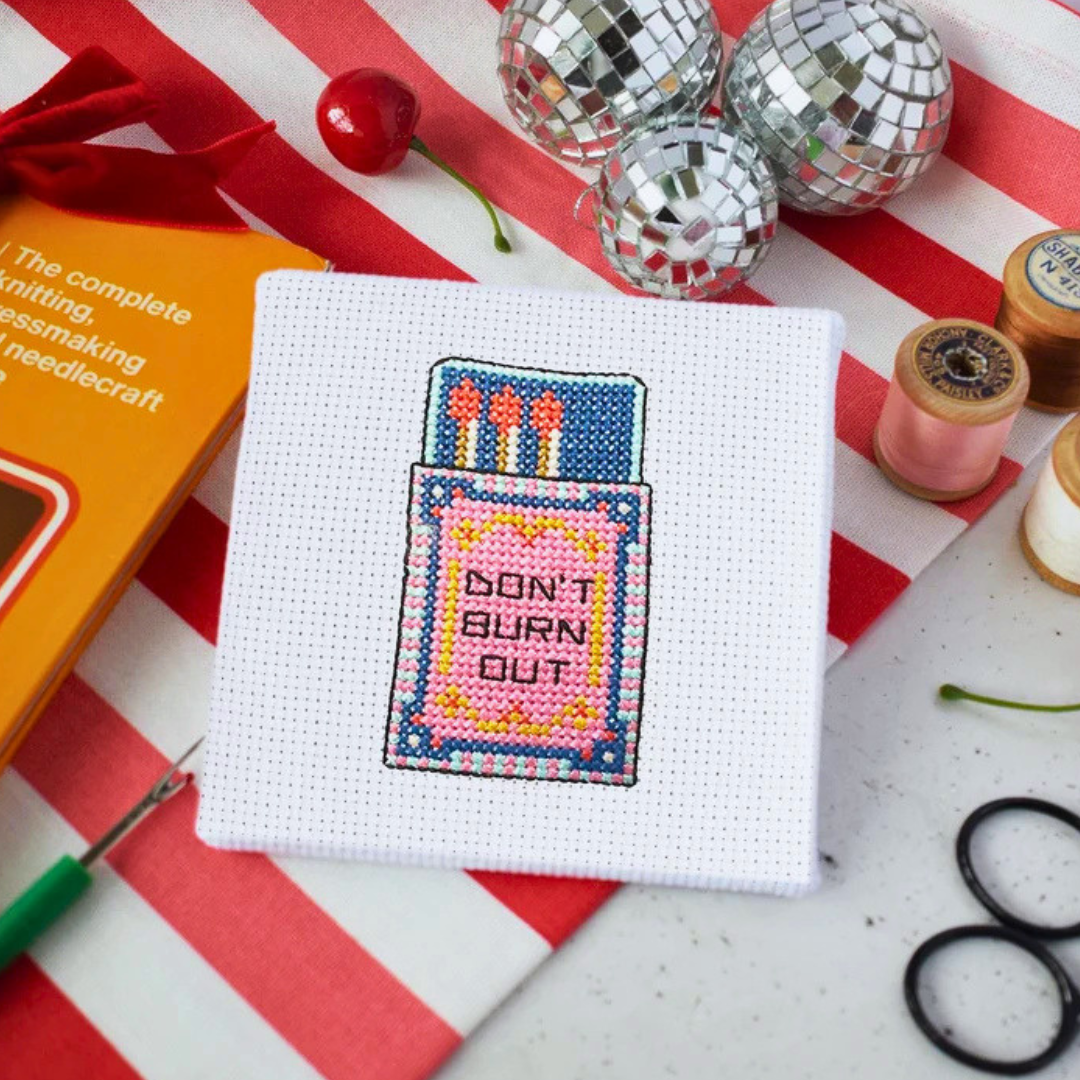 Finished Flamin Hot Mini Cross Stitch Kit displayed with embroidery scissors, thread and colourful craft supplies.