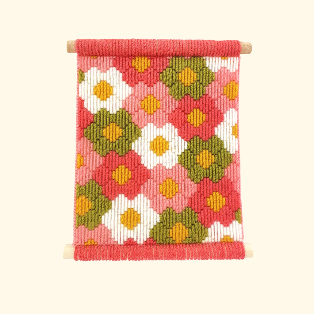 Completed Flower Power bargello wall hanging featuring colourful geometric floral motifs in pink, orange, mustard and green