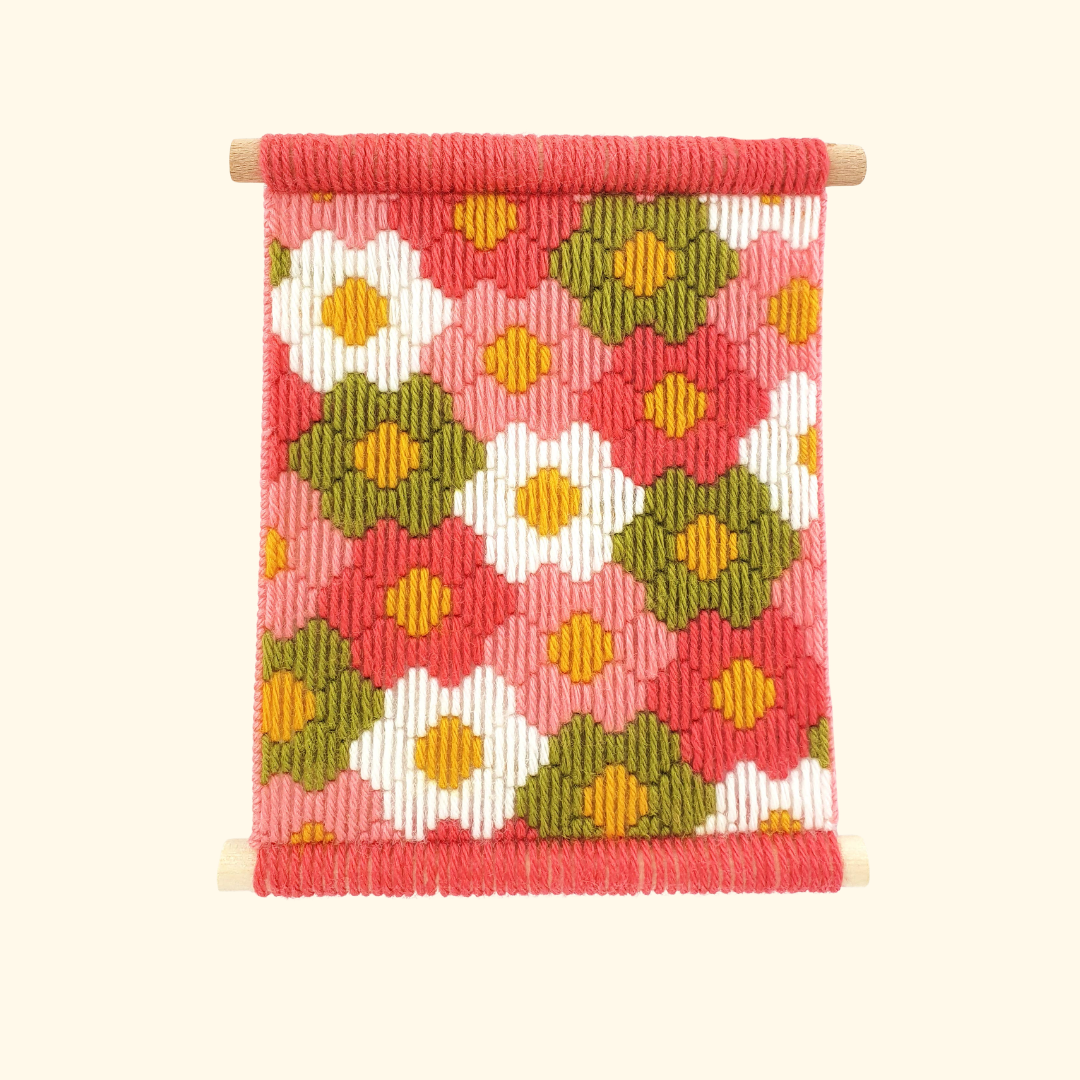 Completed Flower Power bargello wall hanging featuring colourful geometric floral motifs in pink, orange, mustard and green