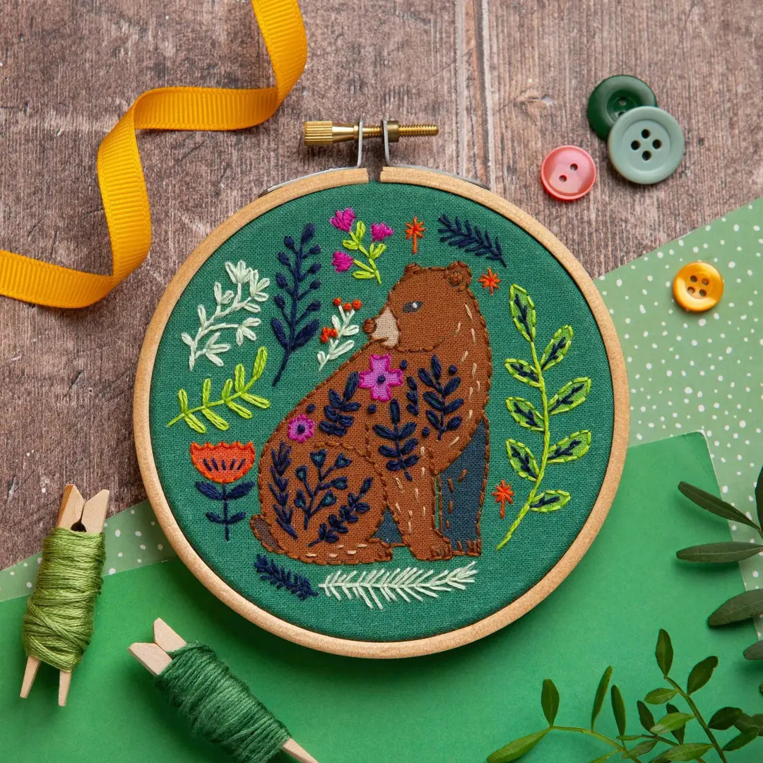 Folk Bear Mini Embroidery Kit in progress with green fabric, wooden embroidery hoop, colourful threads and embroidery accessories.