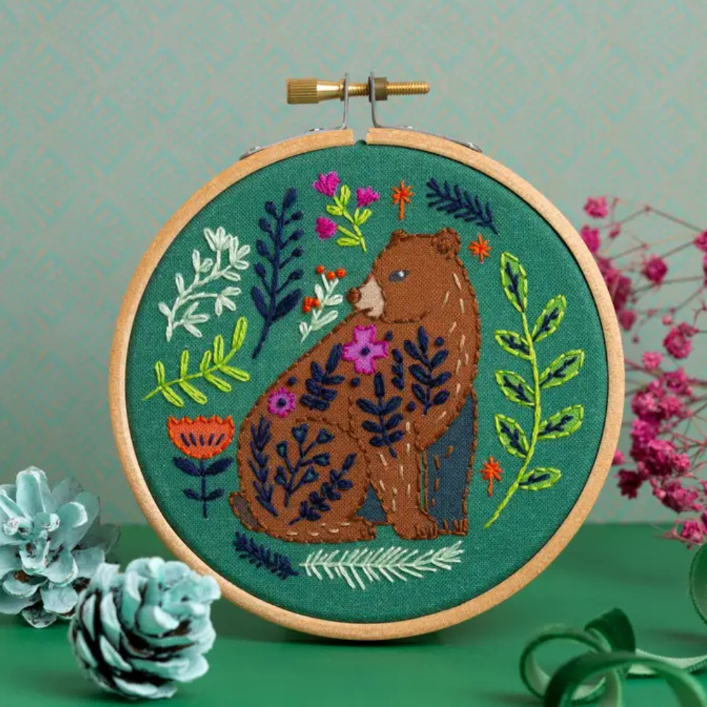 Finished Folk Bear embroidery featuring a bear, flowers and botanical details displayed in a wooden embroidery hoop.