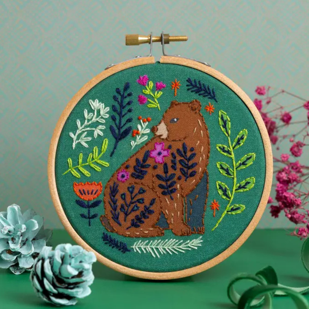 Finished Folk Bear embroidery featuring a bear, flowers and botanical details displayed in a wooden embroidery hoop.