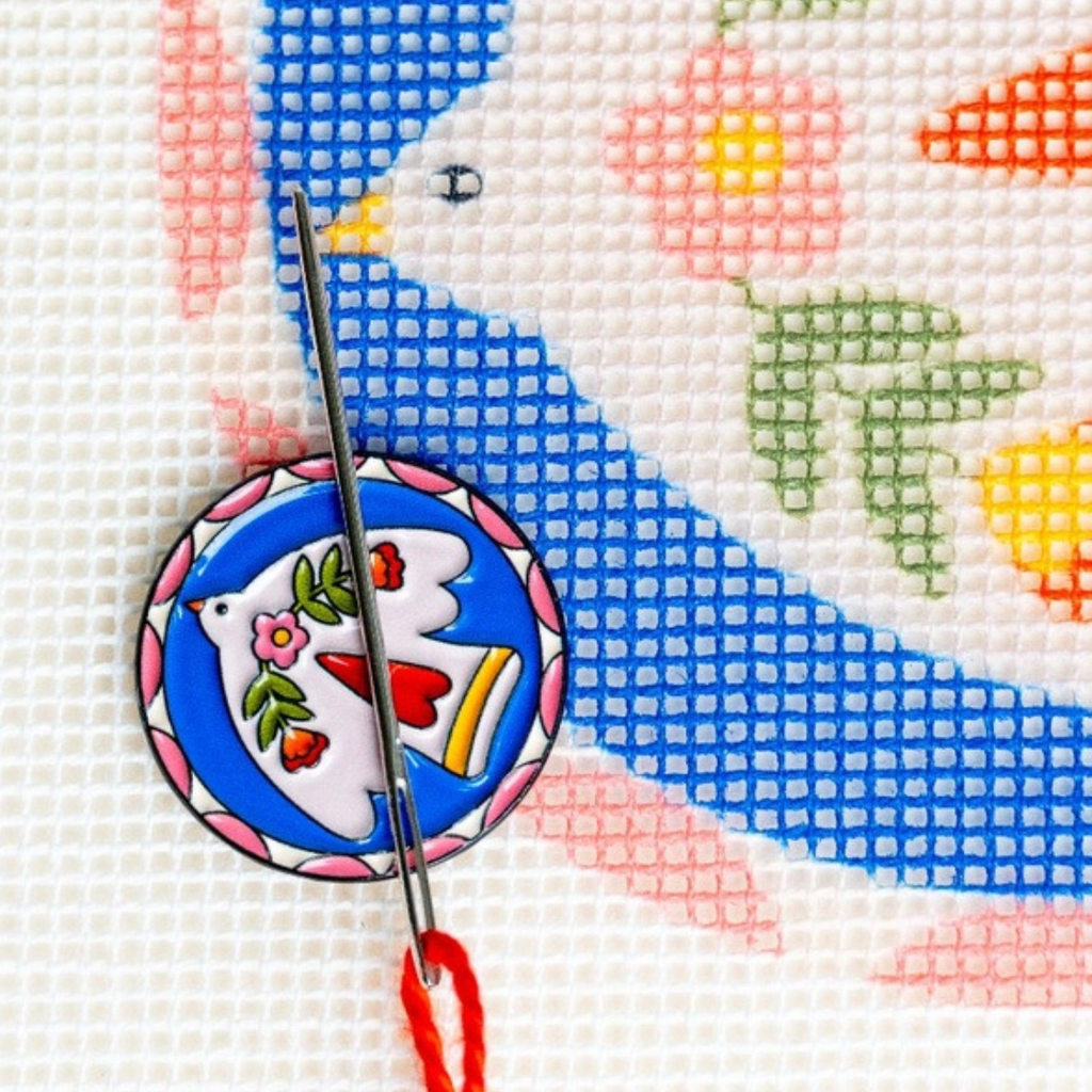 Folk Bird Magnetic Needle Minder holding a needle on a colourful needlepoint canvas during stitching.