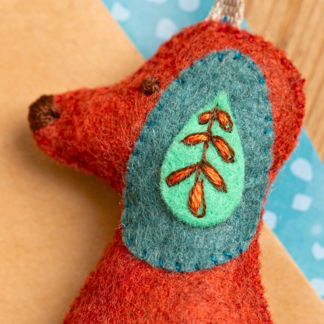 Close-up of the felt dog showing its embroidered face, teal ear and decorative leaf stitching.
