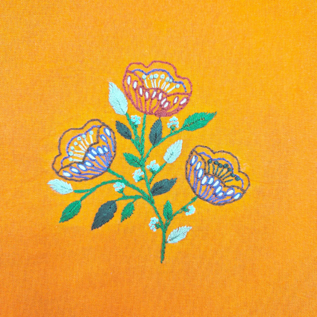 Close up of completed folk flower embroidery stitched onto orange fabric