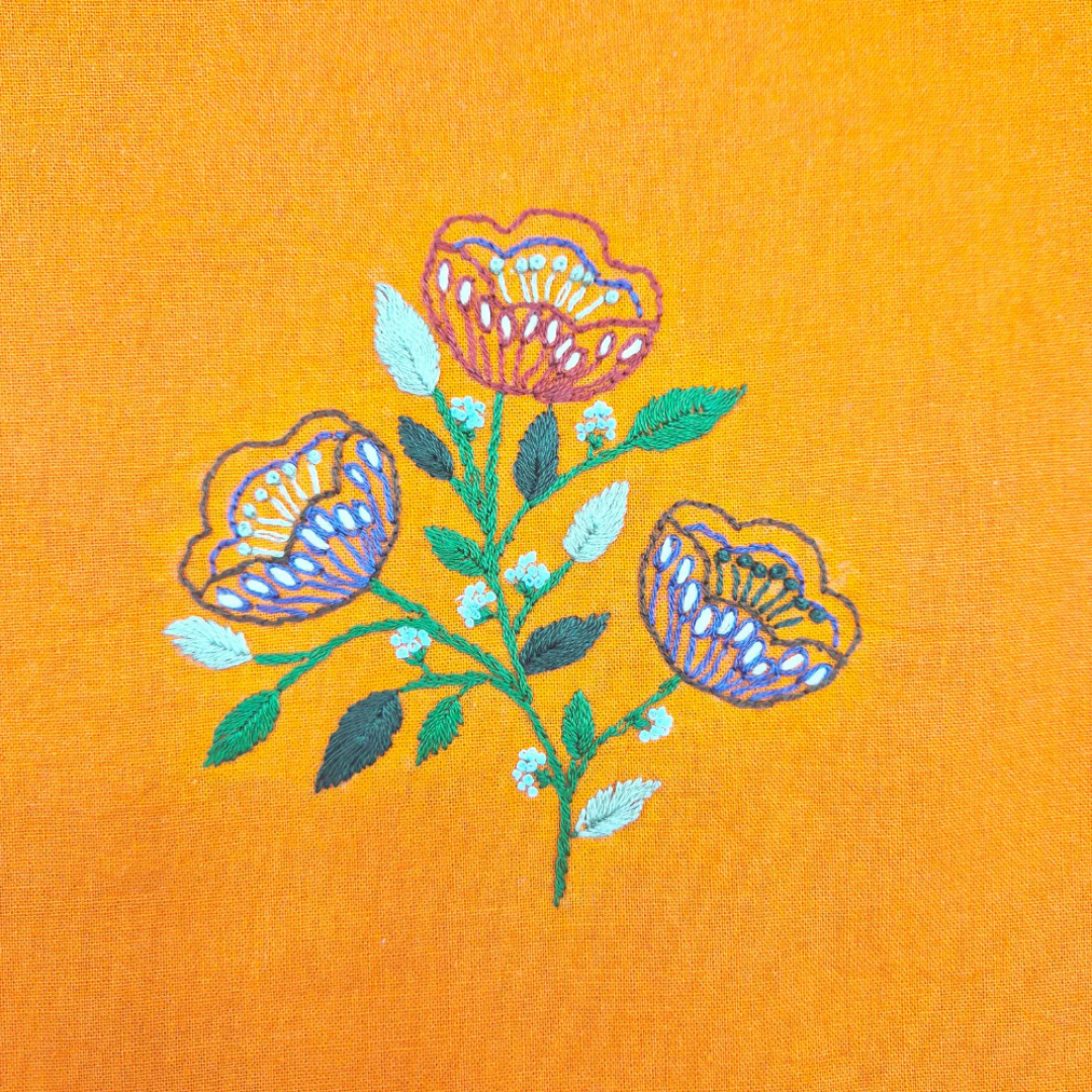 Close up of completed folk flower embroidery stitched onto orange fabric