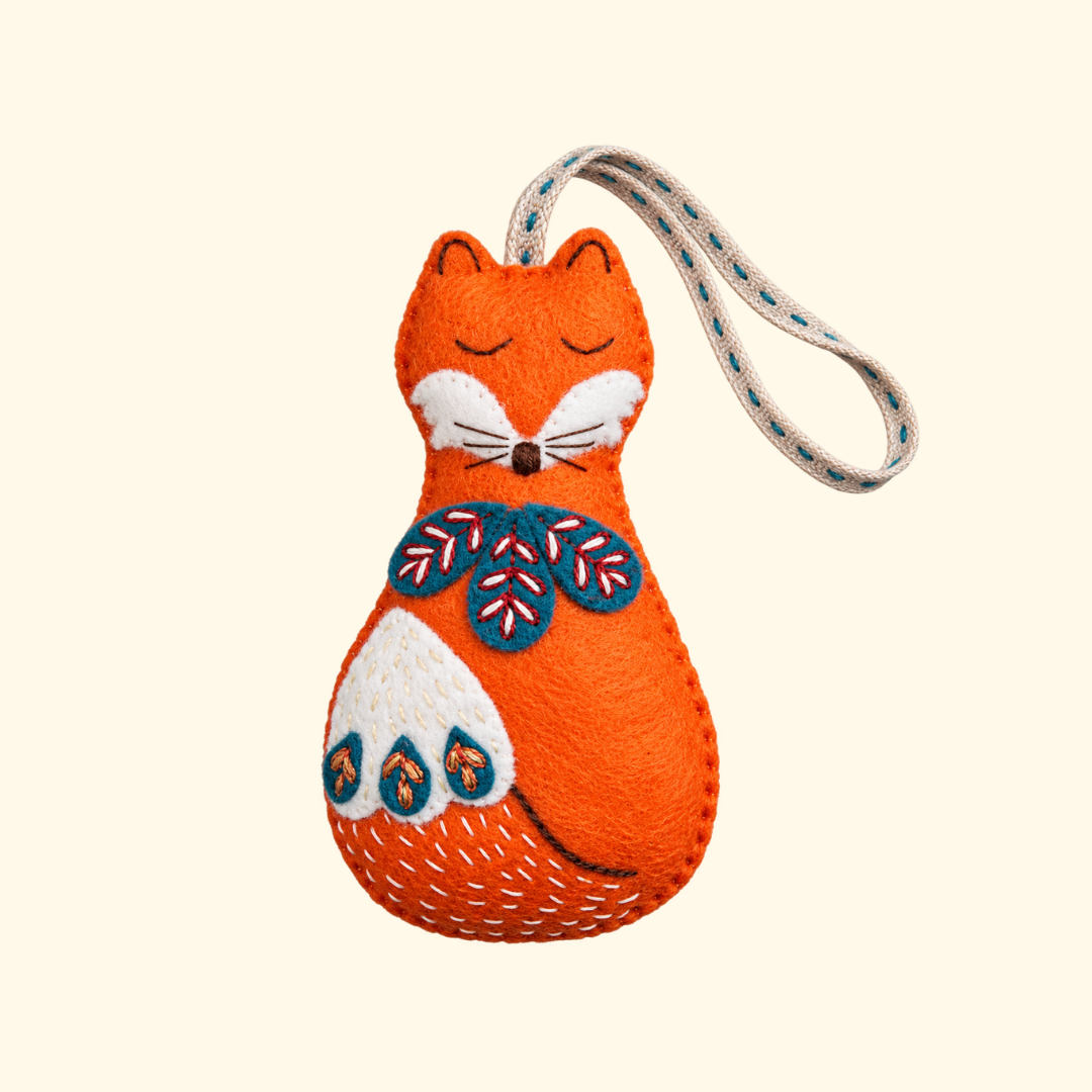 Completed orange felt fox ornament with white face, embroidered blue and red folk details and hanging loop.