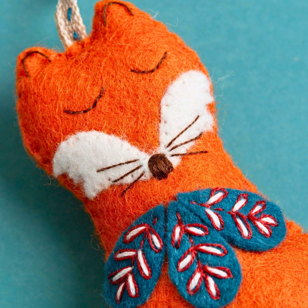 Close-up of the finished felt fox with embroidered face and blue, red and white floral chest detail.