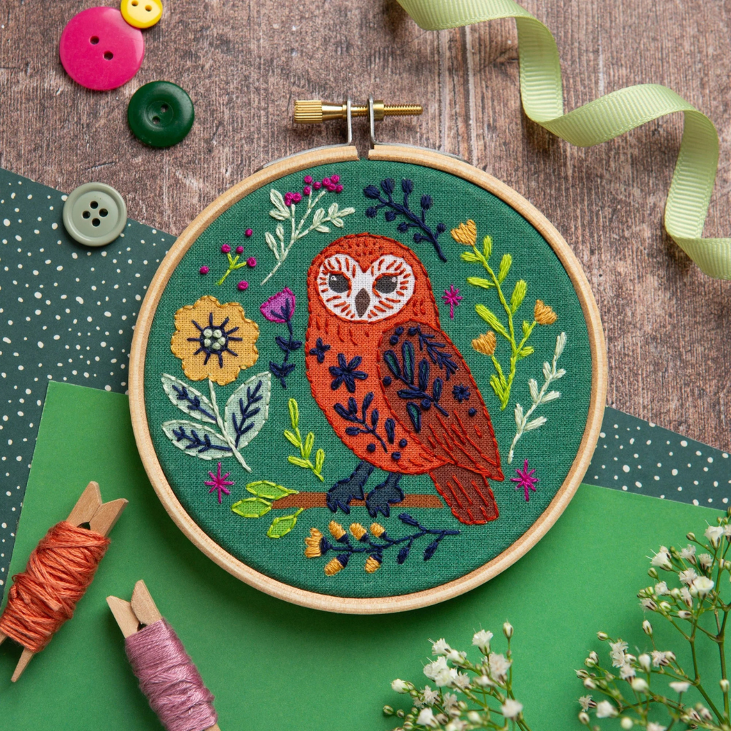 Finished folk owl embroidery hoop styled with flowers and ribbon on a green background.