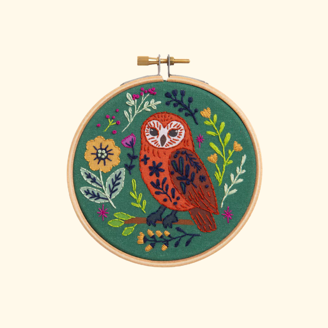Finished folk owl embroidery displayed in a wooden hoop on a plain cream background.