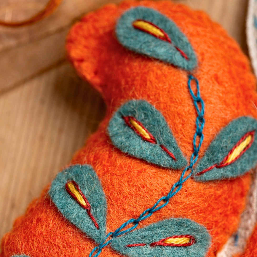Close-up of blue leaf and stem embroidery on the orange felt squirrel craft.