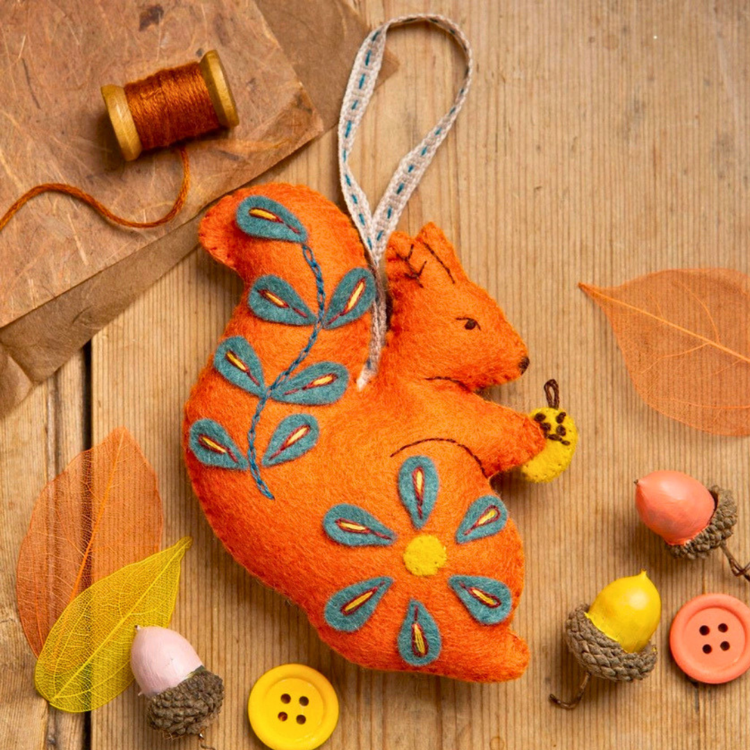 Completed Folk Squirrel felt ornament displayed with thread, buttons and autumn craft decorations.